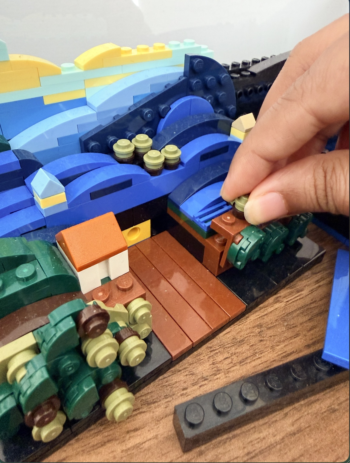A hand adding a piece to a colorful LEGO landscape